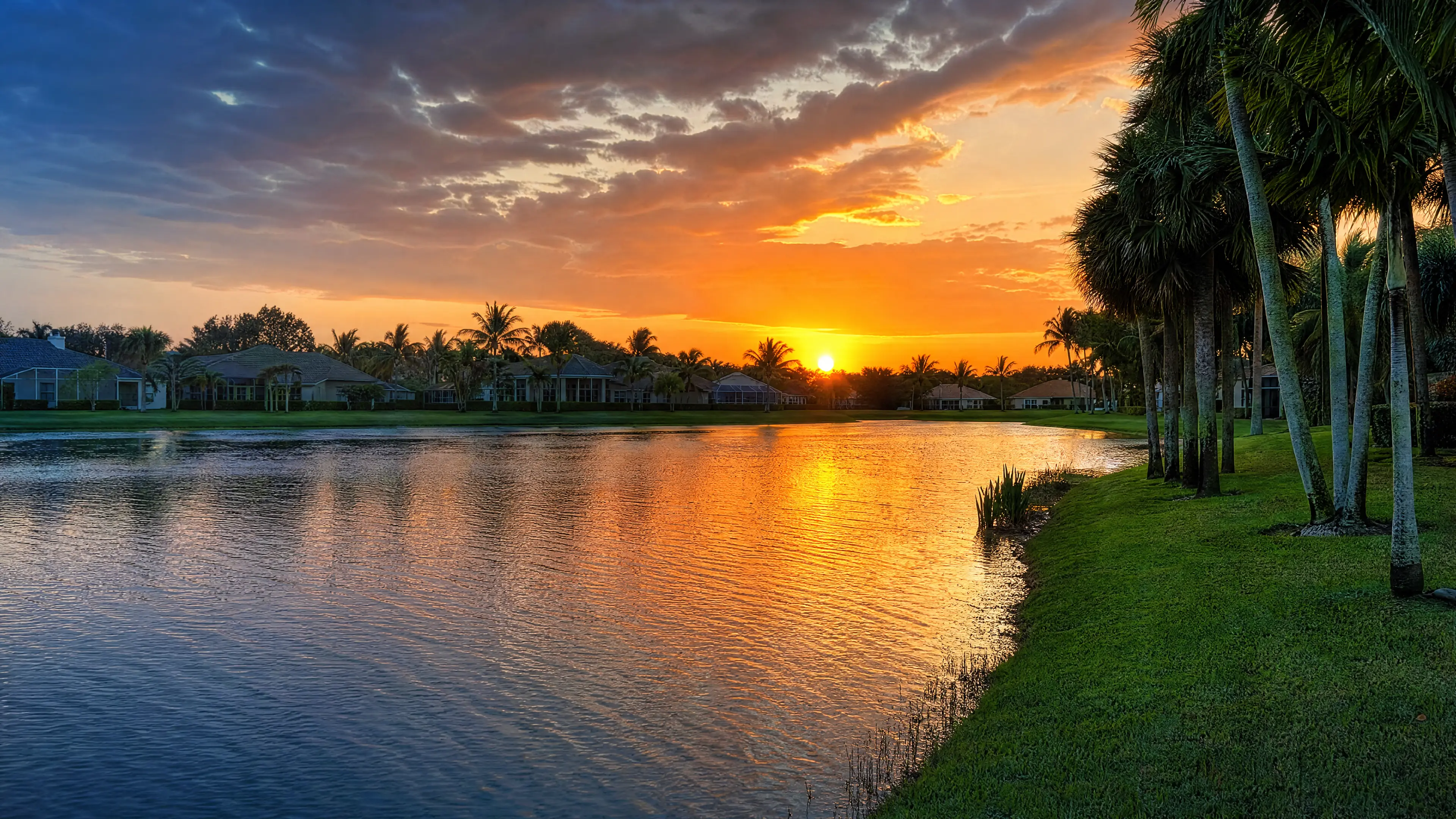 A lakefront Jupiter lawn at sunset with palms reflected in the water